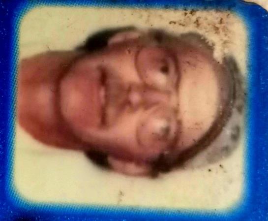 A man with glasses poses for an ID card, showcasing his gray hair and serious expression.