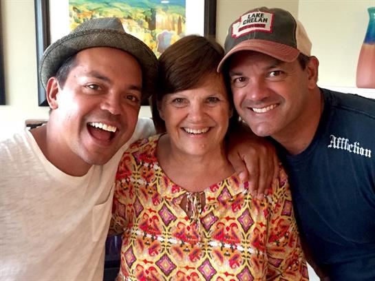 Three cheerful friends smile broadly, sharing warmth at a lively family gathering.