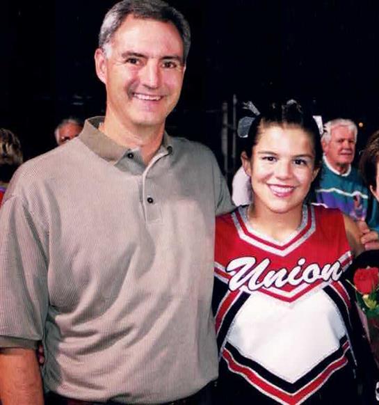 Cheerleader smiles proudly beside her coach at a sports event in a crowded community setting.