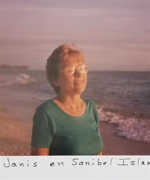 Elderly woman stands on the beach, smiling as ocean waves gently roll toward the shore.