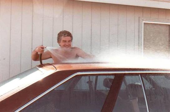 Person cleans a car using a hose while enjoying a sunny afternoon at home.