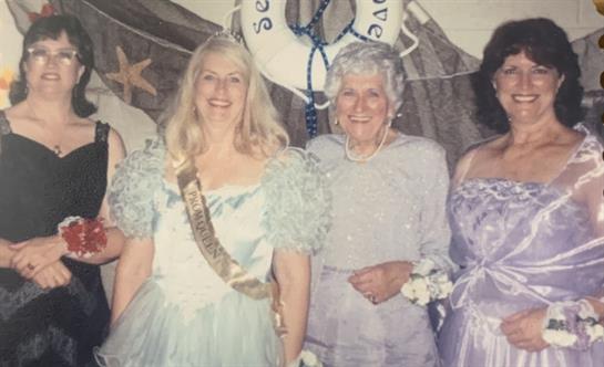 A group of four women are celebrating together in formal dresses at a nautical-themed event.