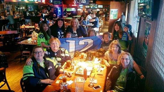Fans gather at a sports bar, cheering, sporting team colors, and enjoying drinks.