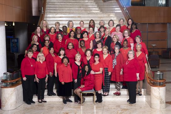 Women dressed in red proudly pose together on a grand staircase to promote heart health awareness.