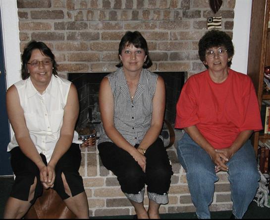 Three women are seated on a low wall near a fireplace, enjoying their time together in a home.