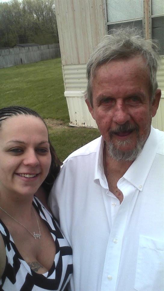 Two individuals take a cheerful selfie in a grassy area near a mobile home during summer.