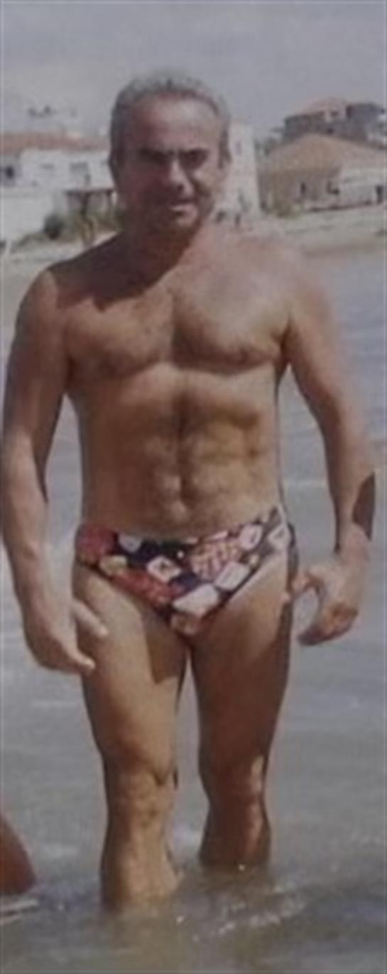 A fit individual walks on the sandy beach in vibrant swimwear under clear skies.