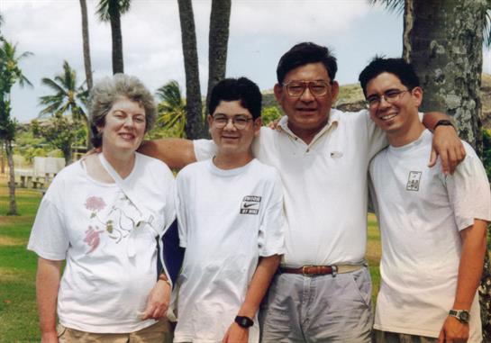 A cheerful family poses together outdoors among palm trees on a bright, sunny day.