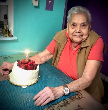 An elderly woman enjoys a birthday celebration at home with a beautifully decorated cake.