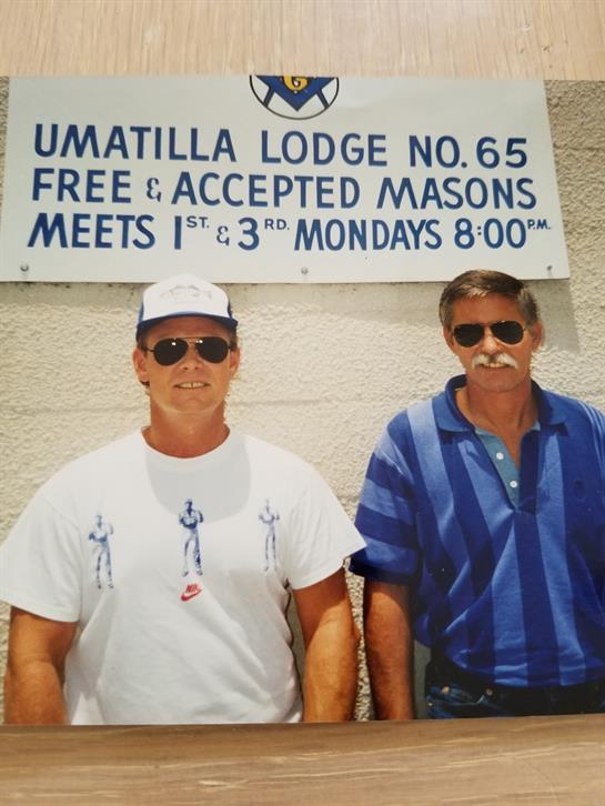 Two men pose in casual attire outside Umatilla Lodge No. 65 under a clear sky.