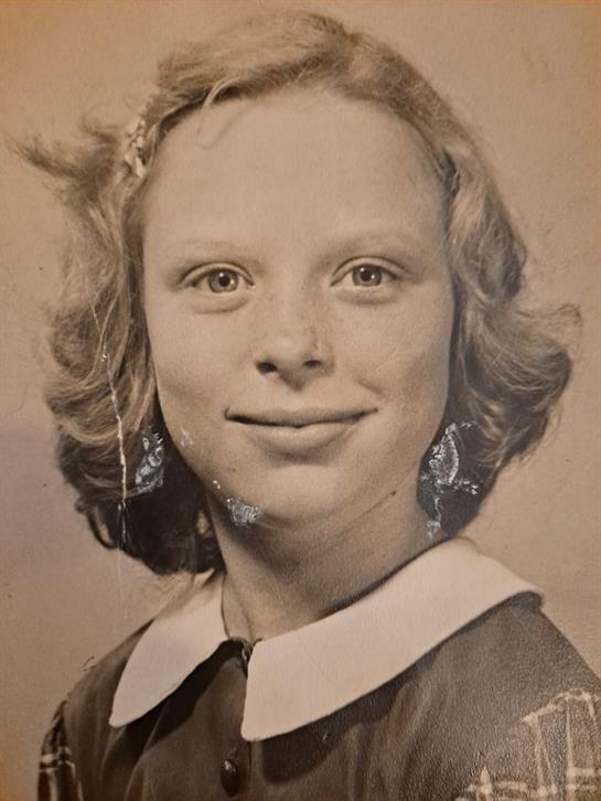 A girl with curly hair and earrings smiles at the camera in a studio, capturing a nostalgic moment.