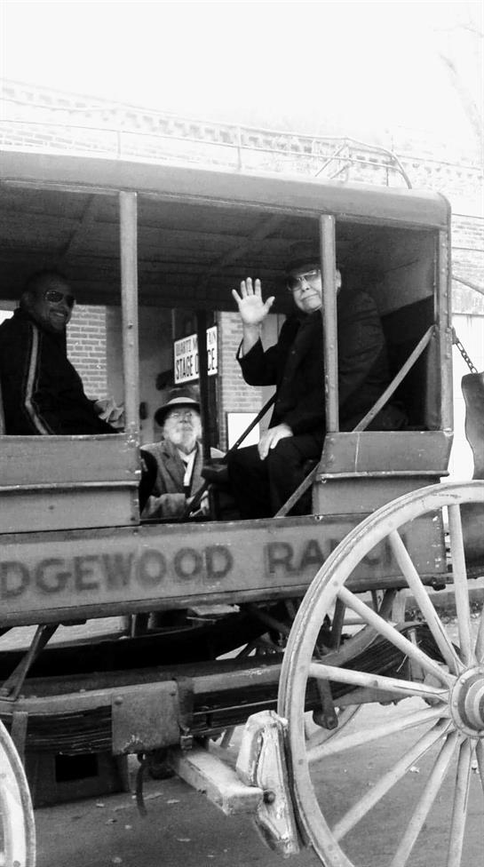 Three men casually interact in a vintage wagon, enjoying the vibrant atmosphere of Ridgewood Rally.