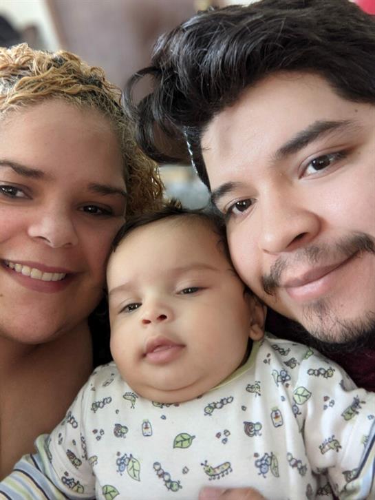 A happy family poses closely together, smiling with their baby in a warm, comfortable environment.