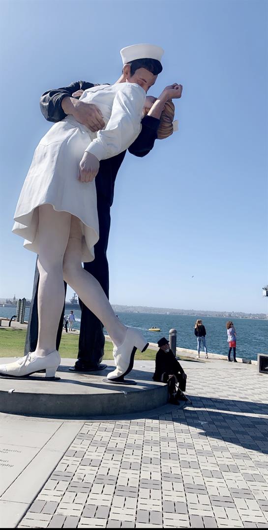 A couple joyfully embraces by the waterfront during daytime, surrounded by onlookers.