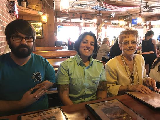 Three individuals sit together at a wooden table in a lively dining establishment, smiling.