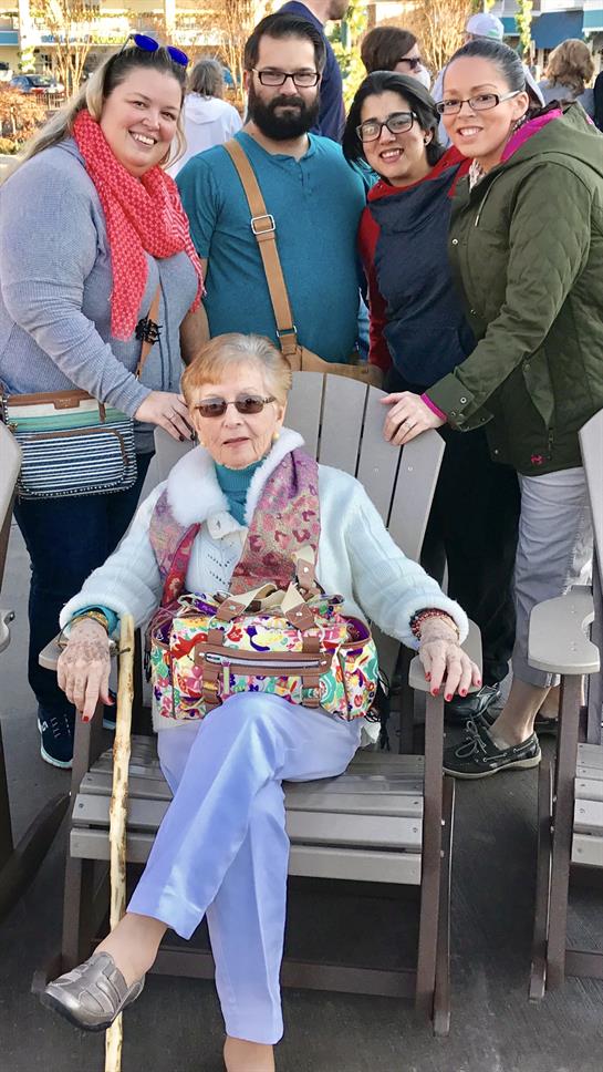 Family members enjoy a sunny day outdoors with an elderly woman seated comfortably in a chair.