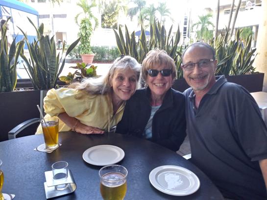 Three friends are seated at a table enjoying drinks and sharing smiles in a vibrant outdoor cafe.