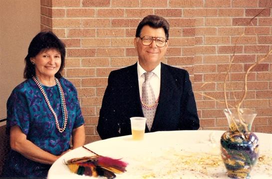 An elegantly dressed couple smiles at the camera from a festively decorated round table.