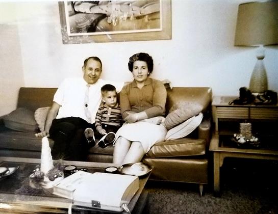 A family of three sits together on a sofa, showcasing love and nostalgia in a cozy living room.