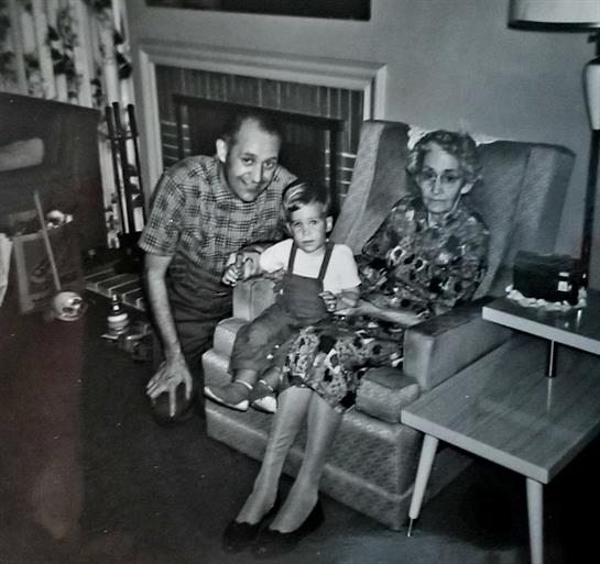 A young girl sits between her grandparents in a warm living space filled with vintage decor.