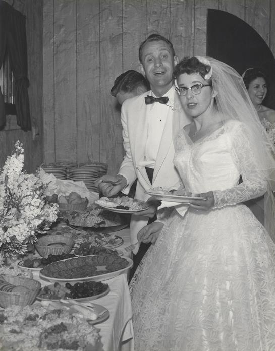 Newlyweds enjoy a festive wedding reception surrounded by tables filled with various dishes.