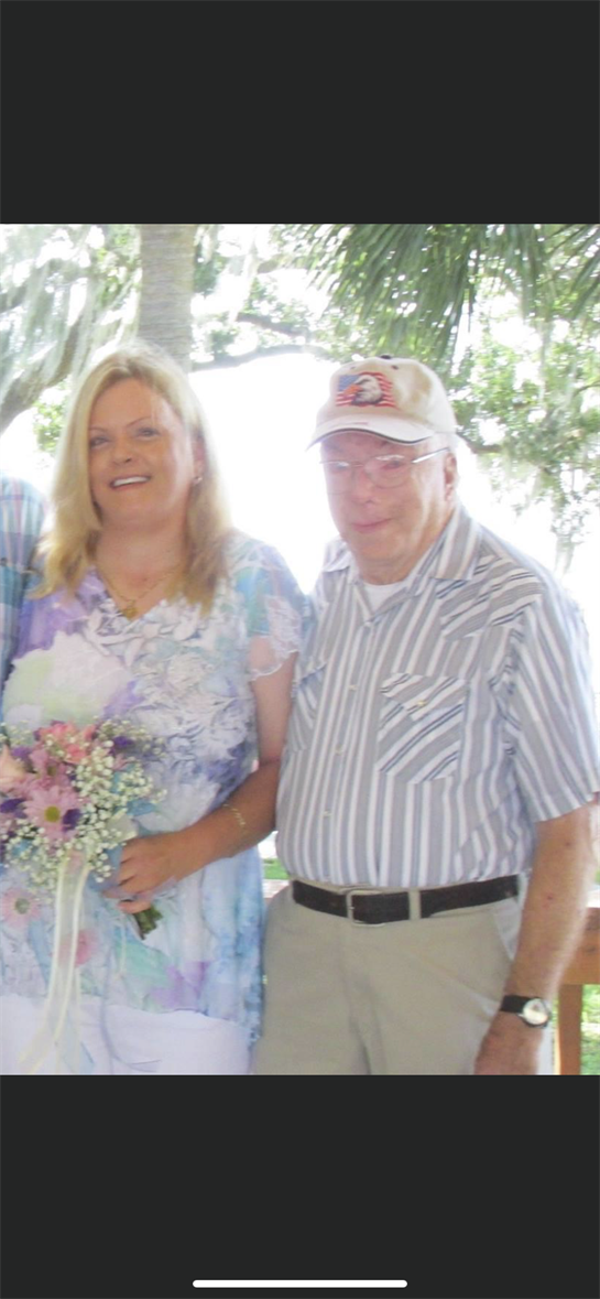 A joyful gathering features two people smiling, one holding a bouquet under a bright sky.