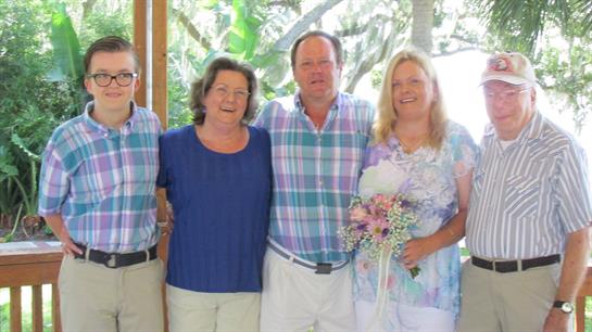 Four adults stand together, smiling and enjoying a festive moment in a tropical location.