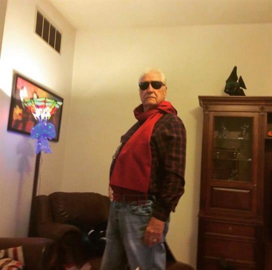 Confident man poses in a cozy living room, wearing sunglasses and a scarf, radiating style.
