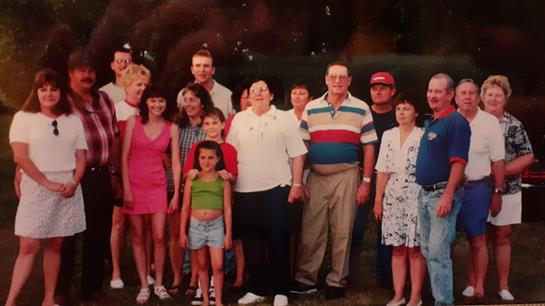 Families of various ages celebrate together in a sunny park while capturing a joyful moment.