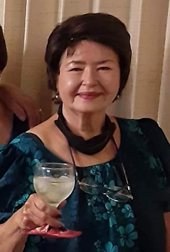 A woman wearing a floral dress raises her glass, smiling joyfully at a festive gathering.