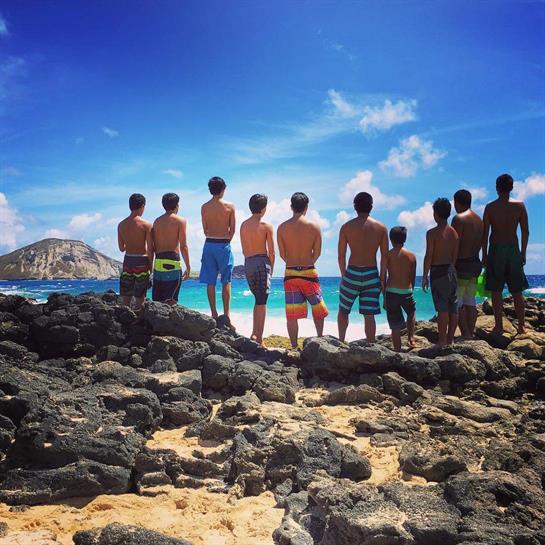 Boys stand together on the rocks, facing the ocean and enjoying the warm sun on a summer day.