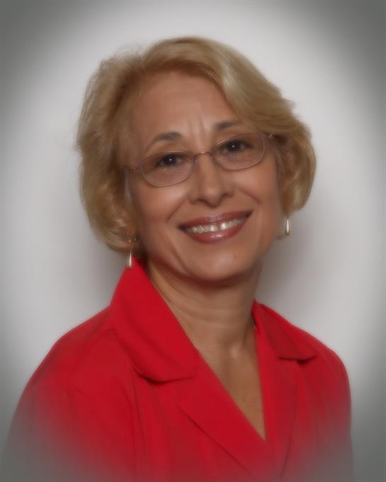 A confident woman wearing a red blouse smiles warmly in a close-up portrait with a soft background.