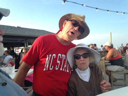Two people enjoy a lively outdoor event, wearing hats and sunglasses under bright sunshine.