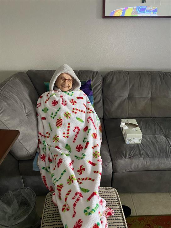 Elderly individual enjoys a moment of comfort sitting on a couch wrapped in holiday-themed warmth.