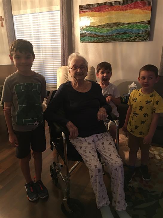 Four children gather around an elderly woman in a wheelchair, sharing smiles in a warm home setting.