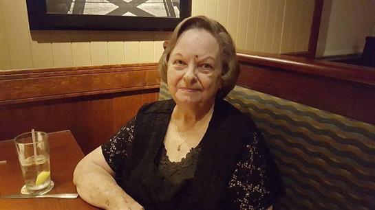 A calm senior woman sits at a table in a cozy restaurant, enjoying her surroundings.
