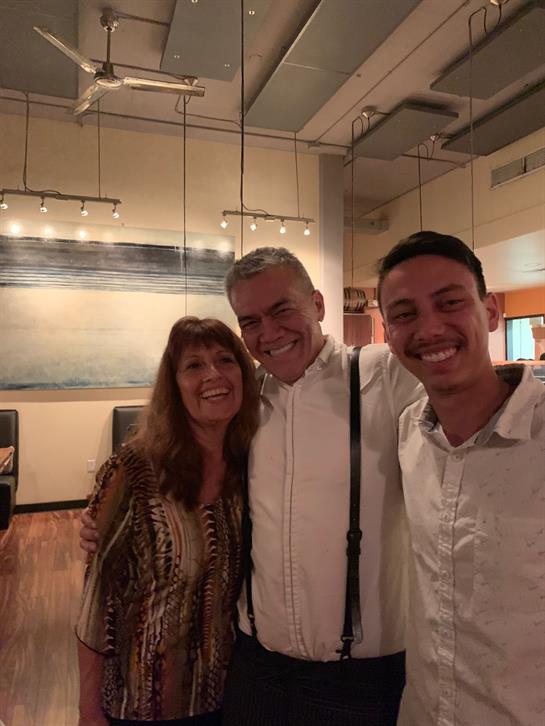 Three friends smile and pose together in a warm restaurant setting filled with soft lights.