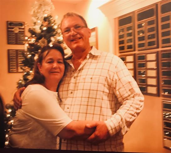 A joyous couple embraces while standing next to a beautifully decorated Christmas tree.