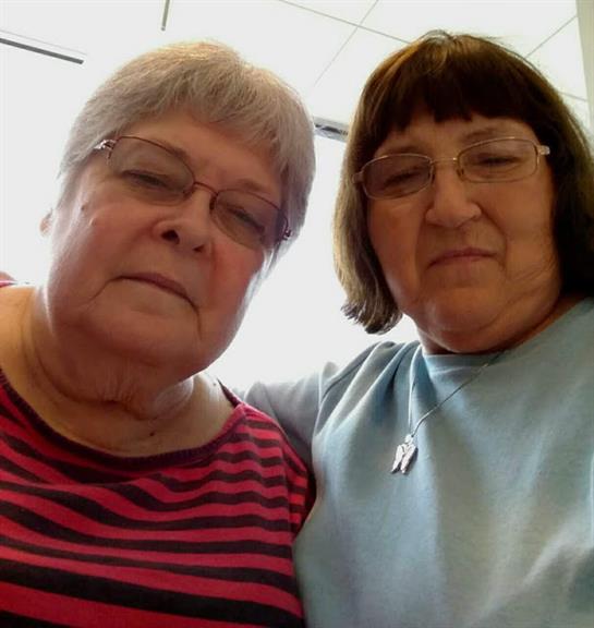 Two women smile as they pose closely together, enjoying their time in a warm environment.