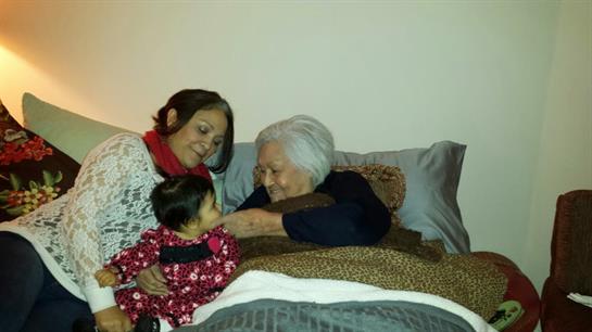 A young child interacts happily with her grandmother while being comforted by her mother.