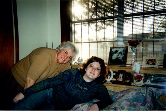 Two friends smile and relax in a brightly lit room filled with personal items and decor.