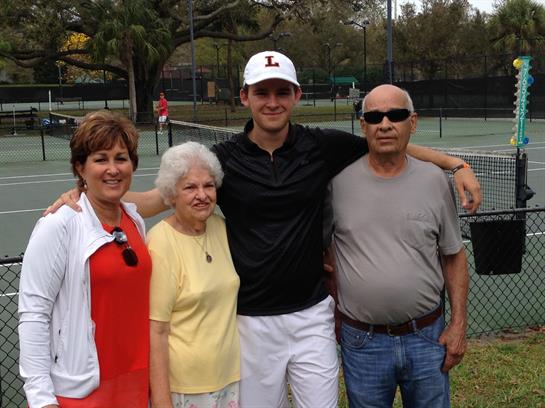 Four people at a tennis court enjoy a sunny day during a family reunion in the park.