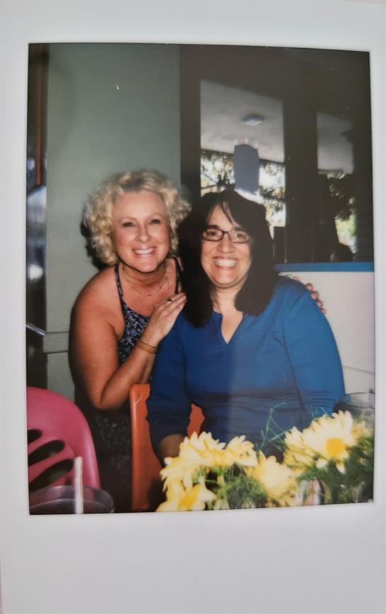 Two smiling women pose together at a restaurant table adorned with yellow flowers.