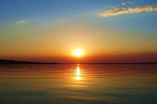 Warm colors fill the sky as the sun sets over still waters, creating a serene atmosphere.