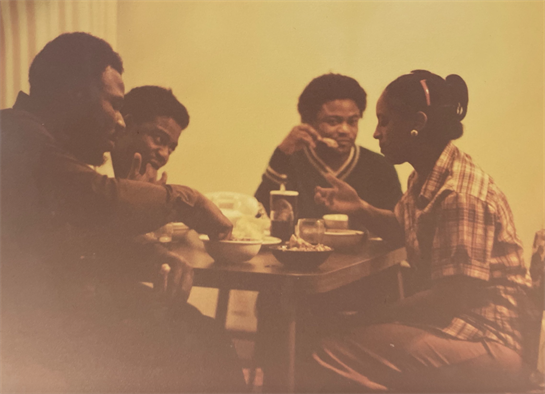 Group of four friends sharing food and laughter at a table in a warm, relaxed atmosphere.