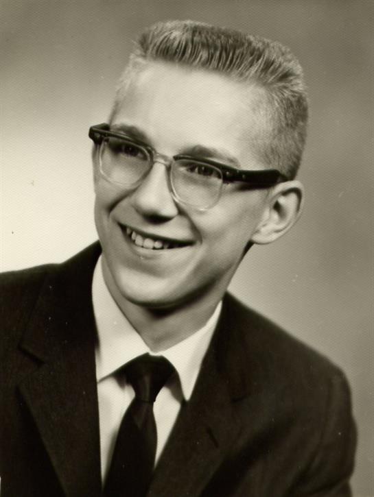 A young man with stylish glasses and a suit is smiling confidently in a vintage portrait.