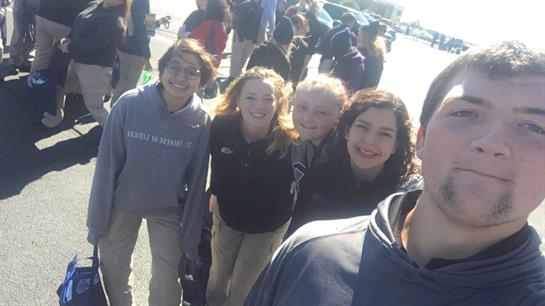 Friends gather and share joyful moments outdoors under bright sunlight during an event.