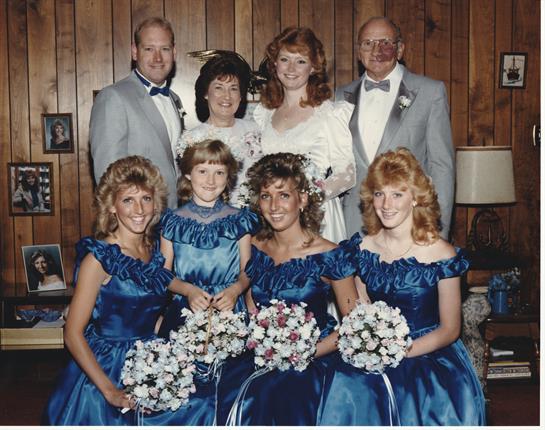Group of friends and family gather for a wedding celebration indoors, showcasing 1980s fashion.