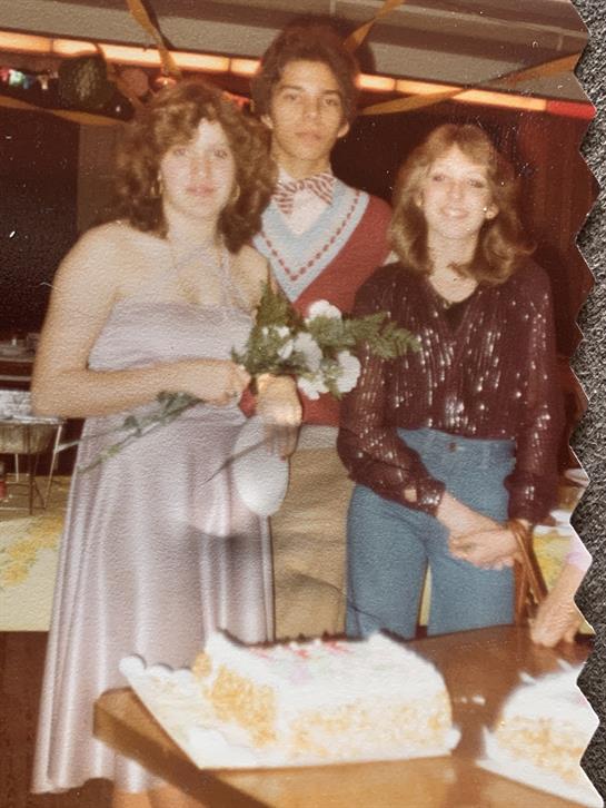 Friends in festive attire gather around a cake to celebrate and enjoy the moment.
