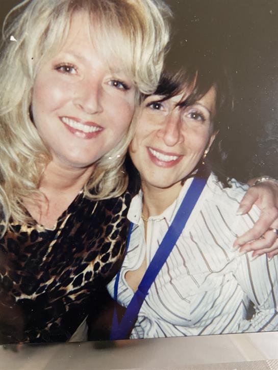 Two friends smile while enjoying a fun night together at a vibrant social event.